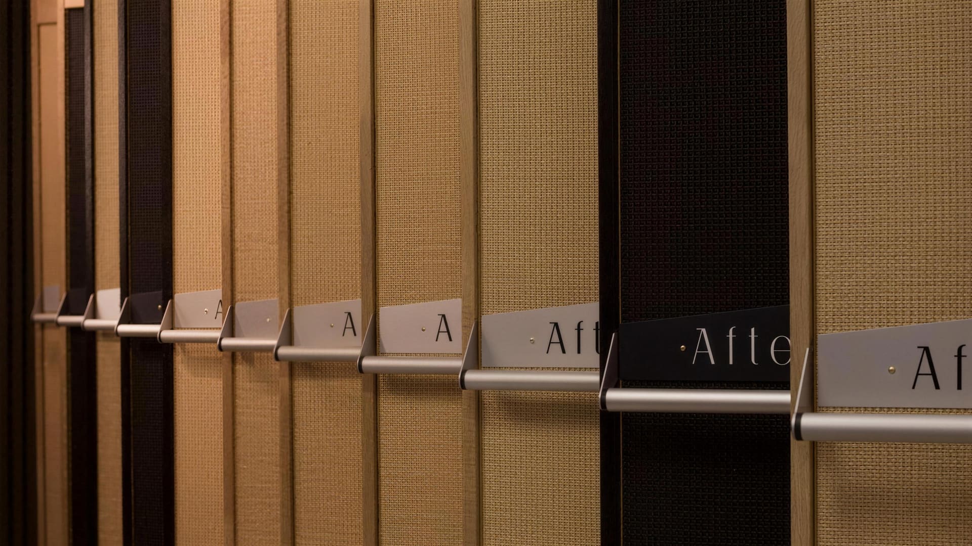 A receding line of Reverbophones along a studio wall, honey oak and black oak frames alternating under warm light, each with a brushed aluminium AfterSound sign on its decay lever